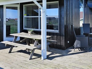 An outdoor wooden deck with a picnic table and chairs, a potted plant, and a view of the surrounding area. - 6 Person Holiday Home in Lemvig (Lemvig)