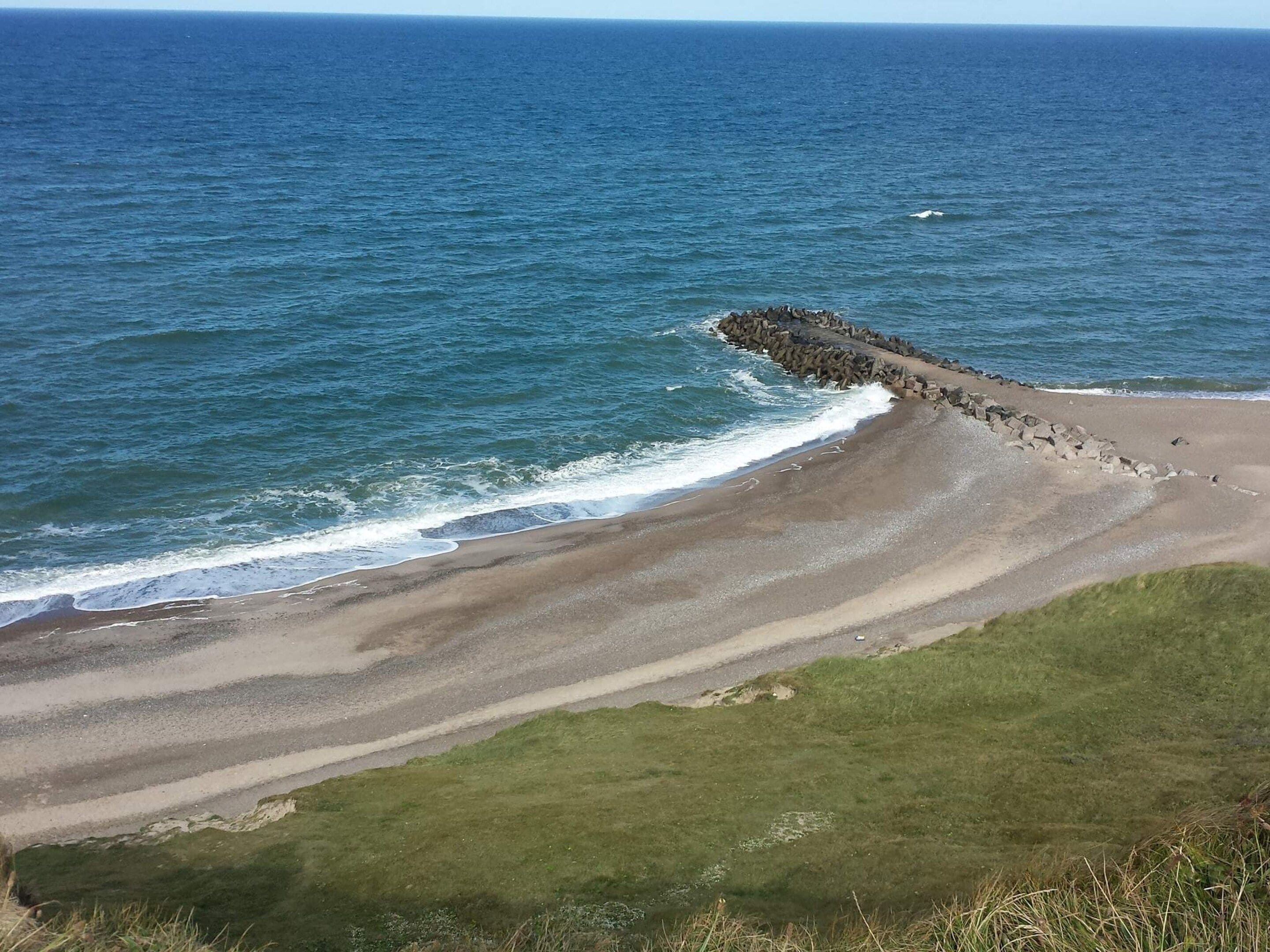 Un paysage côtier avec une plage de sable, une digue rocheuse et l’océan.