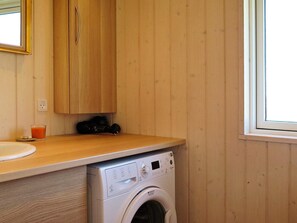 Un área de lavandería compacta con lavadora, armarios de madera y una ventana.