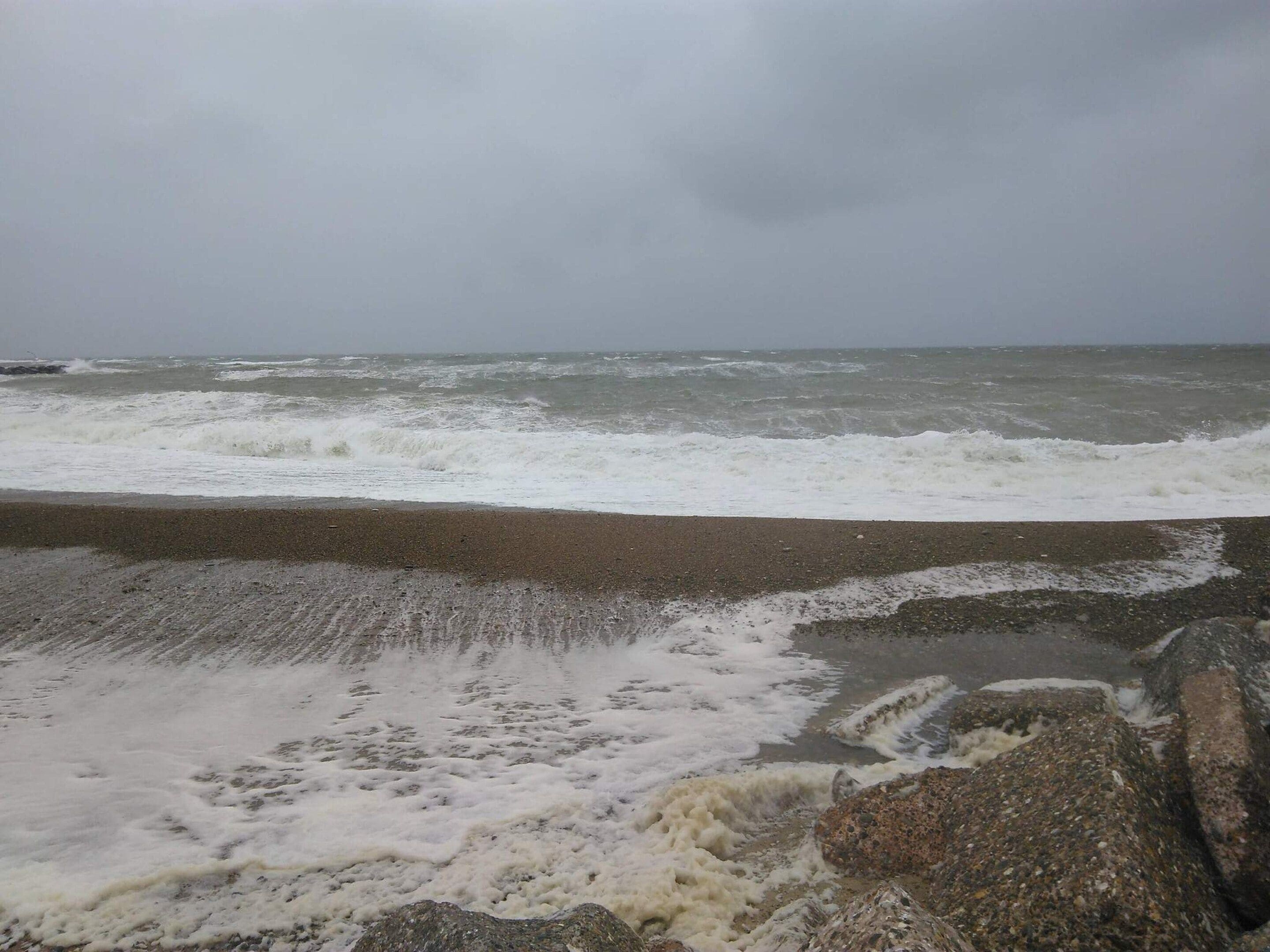 Una playa con olas rompiendo en la orilla, un afloramiento rocoso y un cielo nublado.