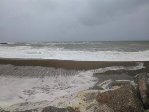 A beach with waves crashing onto the shore, a rocky outcrop, and a cloudy sky.