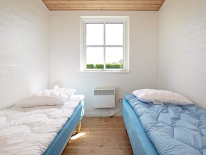 A small, single-room bedroom with two beds, a window, and a wall-mounted air conditioner.