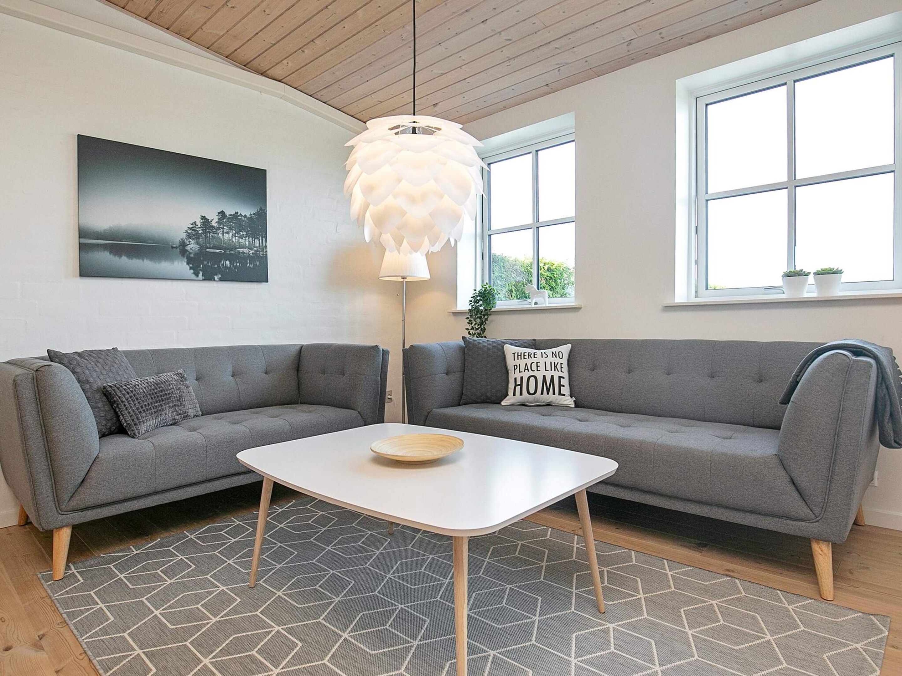 A living room with two grey sofas, a white coffee table, a hanging light fixture, and a painting on the wall.