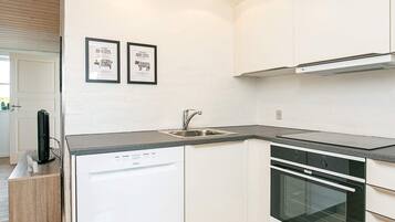 A modern kitchen with white cabinetry, a dishwasher, a sink, and an oven. There are two framed pictures on the wall.