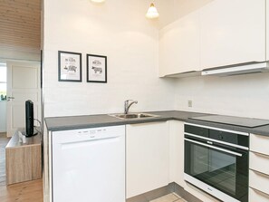 A modern kitchen with white cabinetry, a dishwasher, a sink, and an oven. There are two framed pictures on the wall.