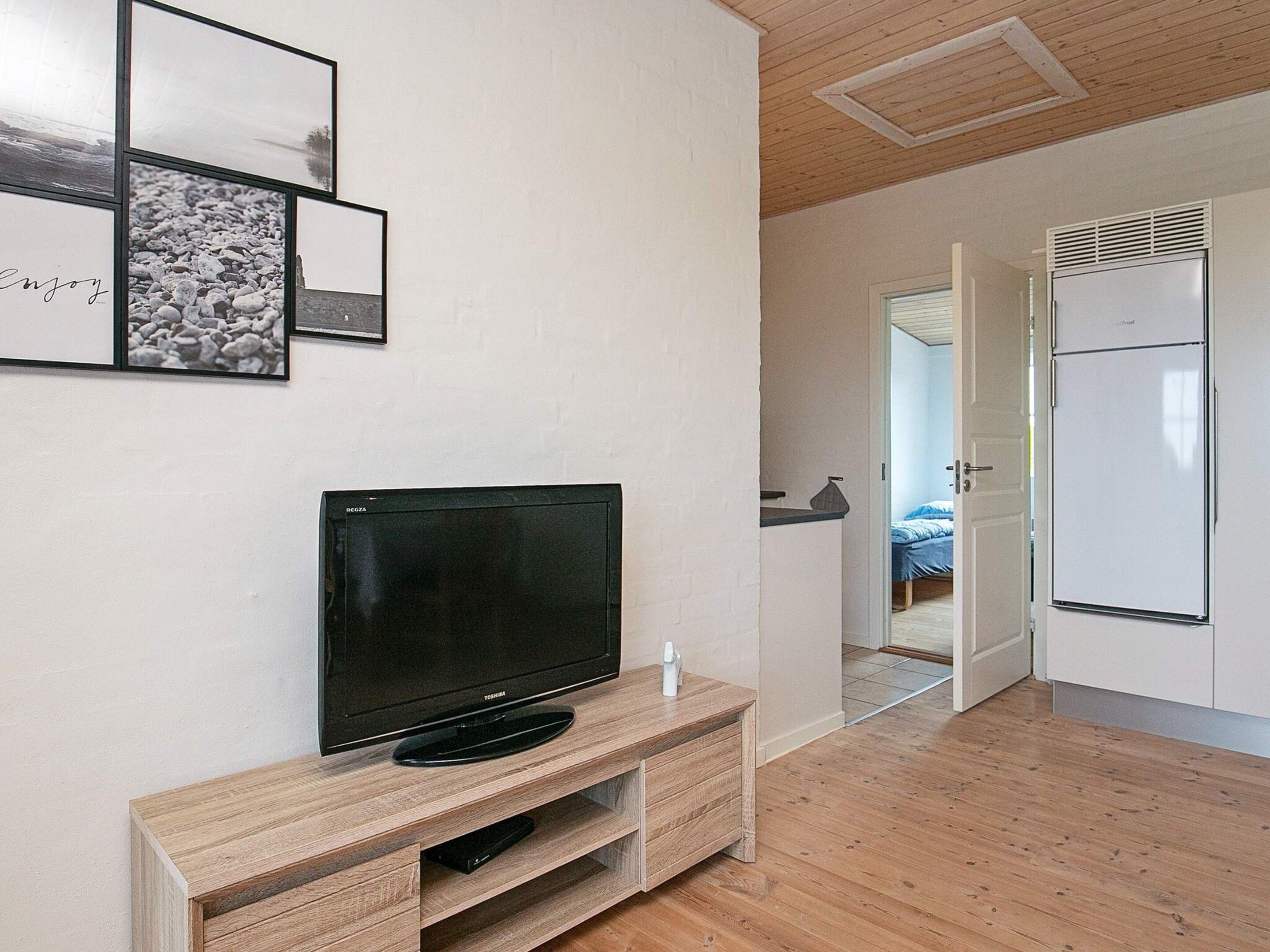 Ein modernes Wohnzimmer mit einem Flachbildfernseher auf einem Holzboden, einer weißen Wand mit gerahmten Bildern und Holzdielen.