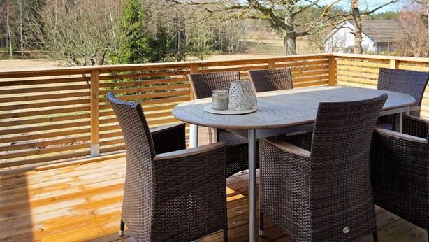 Una terraza de madera con una mesa redonda y sillas de mimbre, con vistas a un paisaje natural.