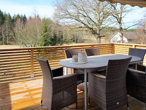 En træterrasse med et rundt bord og fletstole, med udsigt over et naturområde.