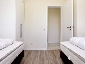 A bedroom with two beds, a wardrobe, and a door leading to another room. - Holiday Home in Grossenbrode (Grossenbrode)