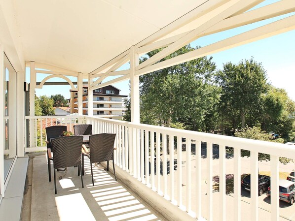 A balcony with wicker furniture and a view of a parking area and buildings. - Holiday Home in Grossenbrode (Grossenbrode)