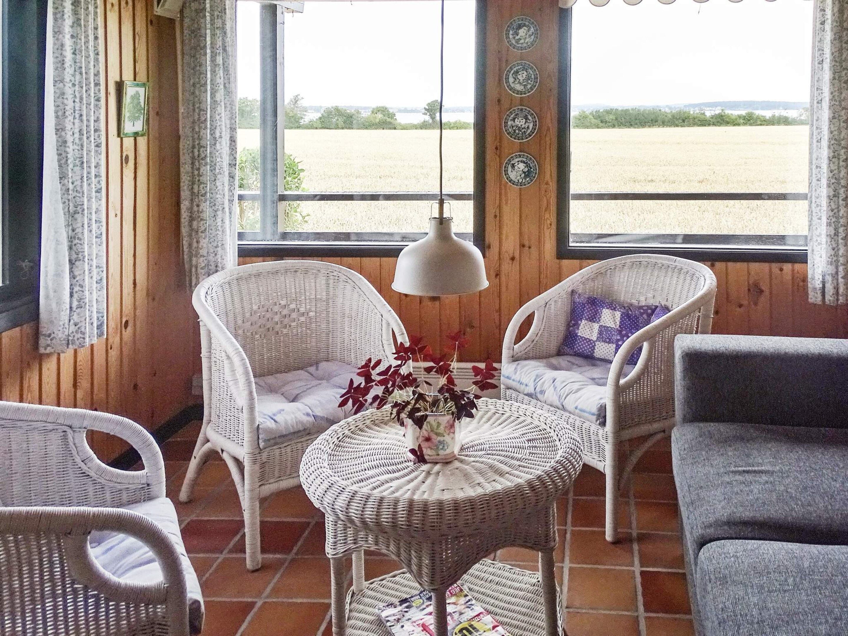 A room with wicker furniture, a table with a vase, and a view of a field through a window.