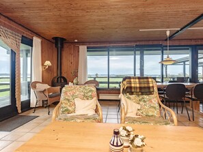 A room with a wooden ceiling, large windows, wicker chairs, a wooden table, and a fireplace. - Alluring Holiday Home in Syddanmark near Sea (Svendborg)
