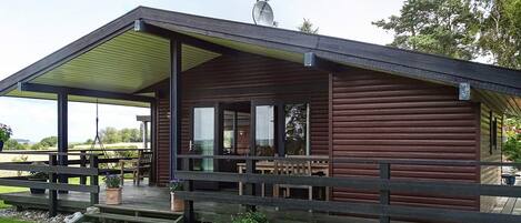 Une cabane en bois dotée d’un porche couvert, d’une antenne parabolique et offrant une vue sur le paysage environnant.