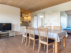 A dining area with a table and chairs, a television, and a kitchen in the background.