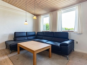 Un salon moderne avec un canapé d’angle, une table basse en bois et deux lampes suspendues.