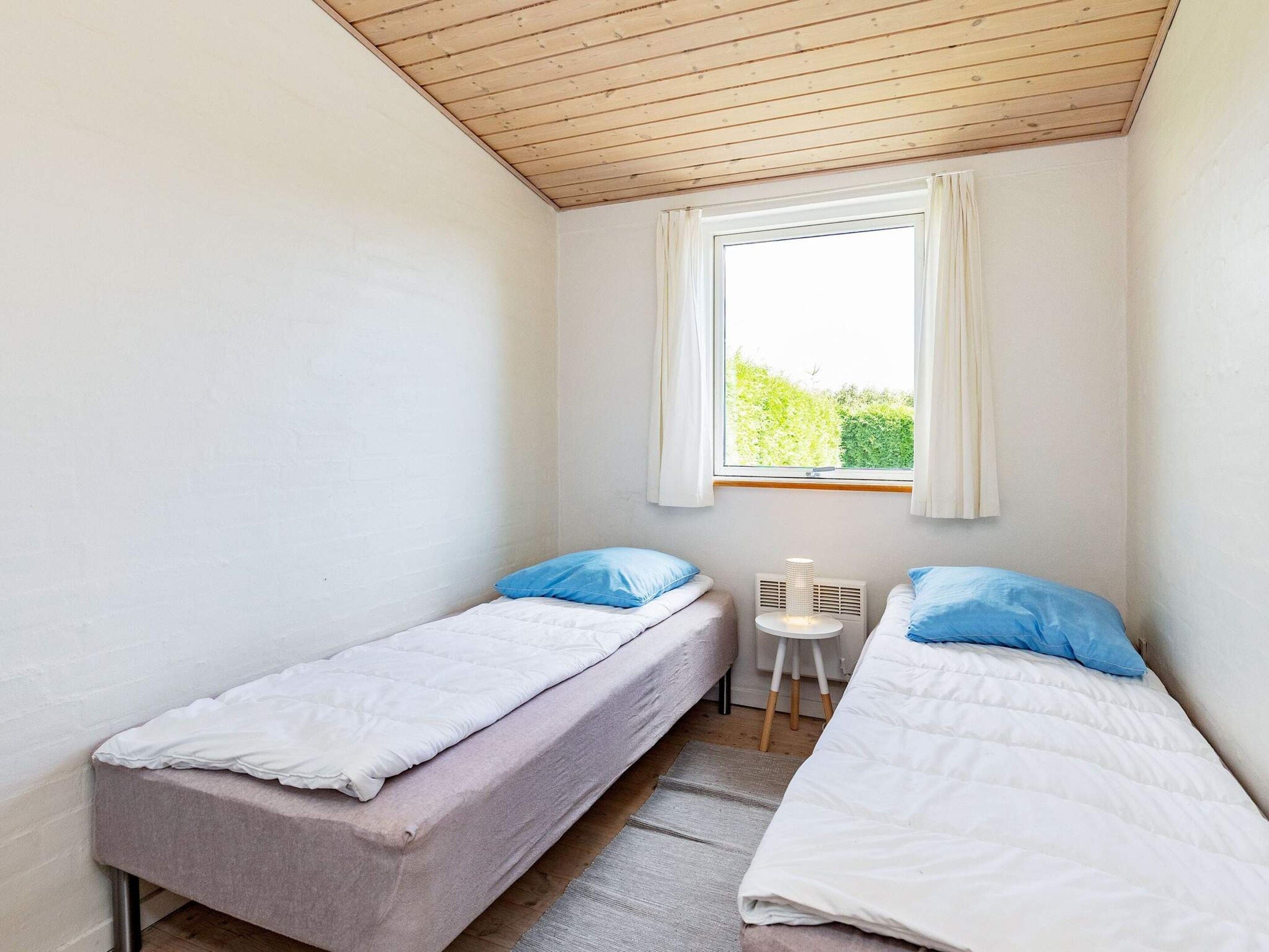 A small, single-room accommodation with two single beds, a window with curtains, a small table, and a radiator.