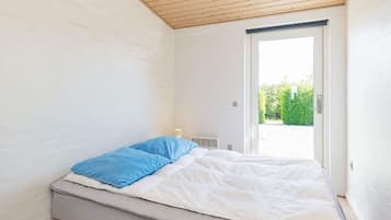 A single bed with a mattress and pillows, a window with a view of greenery, and a wooden ceiling.