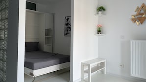 A modern, minimalistic bedroom with a bed, a wardrobe, a small table, and decorative items on the wall. - Westpark 2 Luxury Studio-Suite with Lakeview W5 (Sector 6)