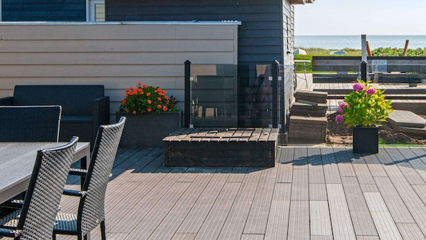 Una terraza de madera con mobiliario exterior y plantas en macetas.