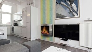 A modern living room with a fireplace, a flat-screen TV, and a dining area with a white table and grey sofas. - Holiday Home in Wendtorf (Wendtorf)