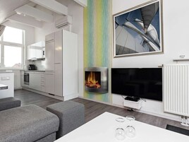 Una sala de estar moderna con chimenea, televisor de pantalla plana y comedor con mesa blanca y sofás grises.