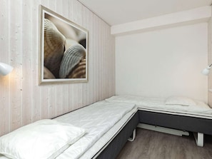 A bedroom with a bed, a nightstand, a wall-mounted lamp, and a framed picture.