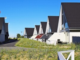 Una hilera de casas modernas con tejados inclinados, una carretera pavimentada y un área verde al frente.