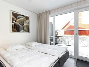 A modern hotel room with a large bed, a sliding glass door to the outside, and a framed artwork on the wall.