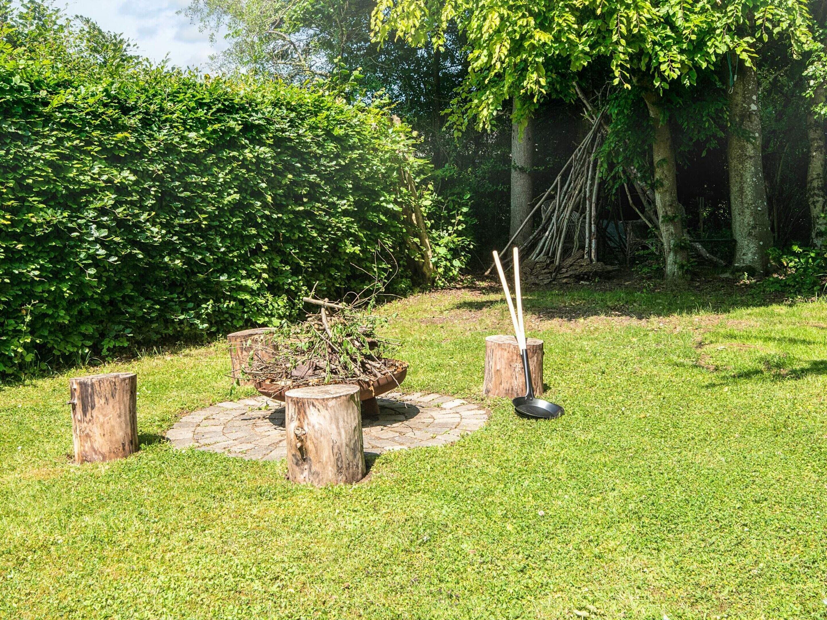A garden with a rustic outdoor seating area featuring a wooden table, chairs, and a fire pit.