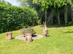 A garden with a rustic outdoor seating area featuring a wooden table, chairs, and a fire pit.