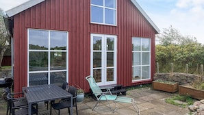 A red wooden house with large windows and a patio area with a table and chairs. - 6 Person Holiday Home in Store Fuglede (Store Fuglede)
