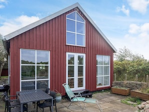 A red wooden house with large windows and a patio area with a table and chairs. - 6 Person Holiday Home in Store Fuglede (Store Fuglede)