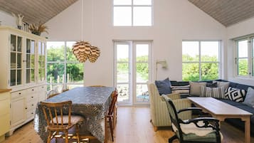 A spacious room with a high ceiling, a dining table with chairs, a sofa, and a wooden floor.