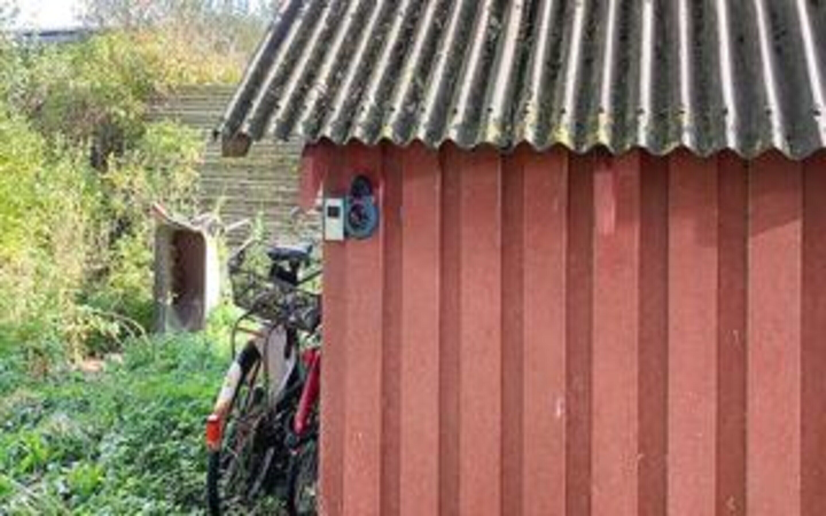 A red building with a corrugated metal roof, a bicycle parked outside, and a small sign on the wall.