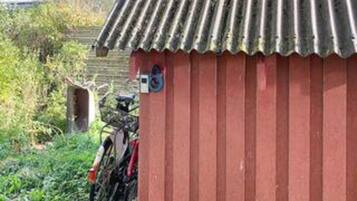 A red building with a corrugated metal roof, a bicycle parked outside, and a small sign on the wall.