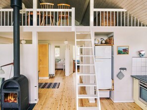 A loft-style room with a black wood-burning stove, a white staircase, and a kitchen area with a refrigerator and a stove. - 6 Person Holiday Home in Store Fuglede (Store Fuglede)