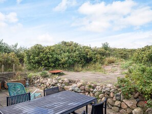 An outdoor seating area with a table and chairs, surrounded by a stone wall and dense foliage.