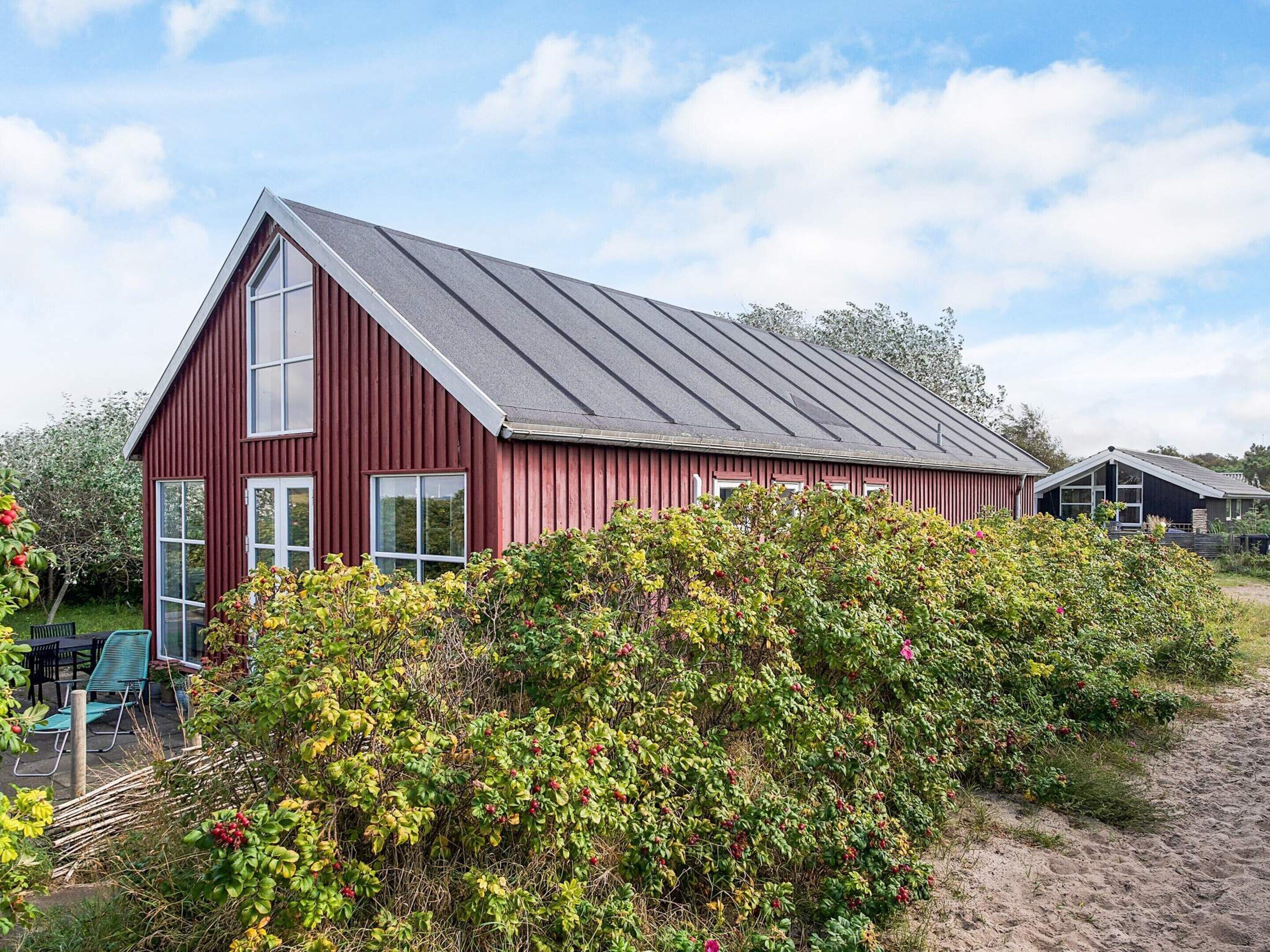 Ein rot gestrichenes Bauernhaus mit Satteldach, umgeben von üppiger Vegetation und einem Sandweg.