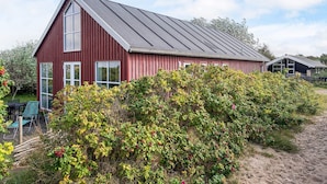 Ein rot gestrichenes Bauernhaus mit Satteldach, umgeben von üppiger Vegetation und einem Sandweg.