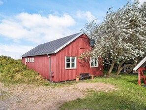 A red wooden house with a sloped roof, a bench, and a tree with white blossoms. - 6 Person Holiday Home in Store Fuglede (Store Fuglede)