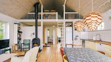 A spacious loft-style living area with a high ceiling, a central fireplace, a dining table, and a kitchen area with wooden accents.
