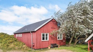 A red wooden house with a sloped roof, a bench, and a tree with white blossoms. - 6 Person Holiday Home in Store Fuglede (Store Fuglede)