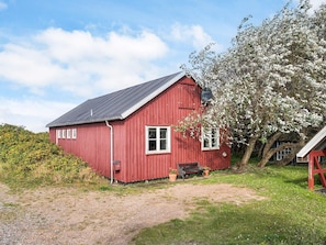 A red wooden house with a sloped roof, a bench, and a tree with white blossoms. - 6 Person Holiday Home in Store Fuglede (Store Fuglede)