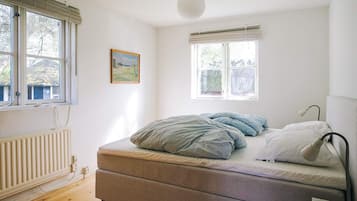 A bedroom with a bed, a radiator, a window, and a hanging light fixture.