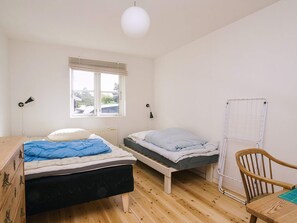 Een kleine, lichte kamer met twee eenpersoonsbedden, een houten stoel, een radiator en een raam.