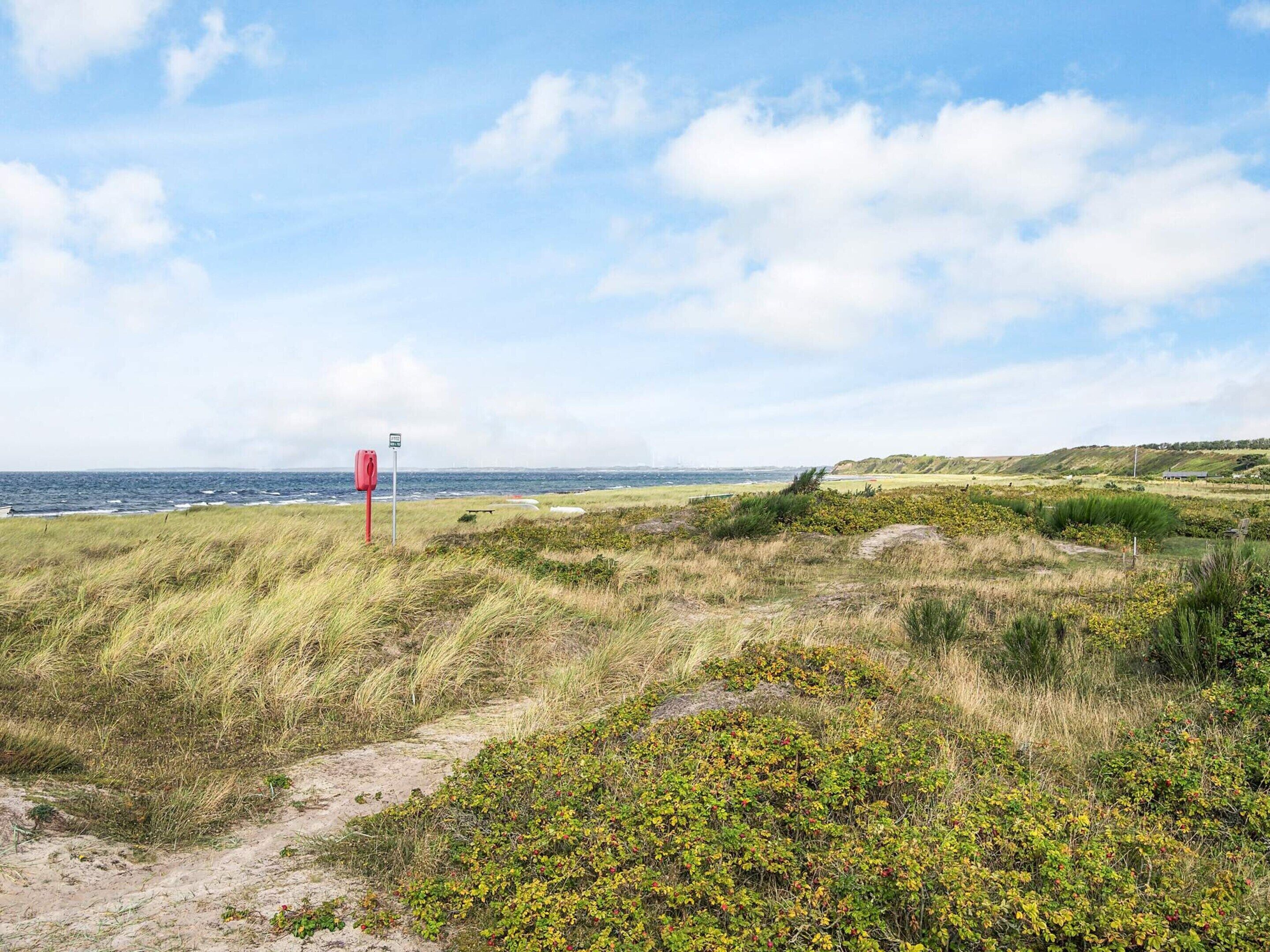 A coastal landscape with a red signpost, grassy dunes, and a view of the sea.