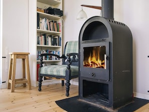A cozy room with a wood-burning stove, a bookshelf, a chair, and a wooden stool. - 6 Person Holiday Home in Store Fuglede (Store Fuglede)