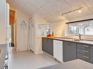 A modern kitchen with a large window, a built-in dishwasher, and a fruit bowl on the counter.