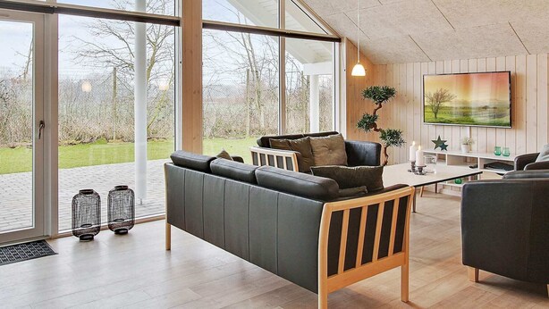 A spacious living room with large windows, a sofa, a coffee table, and a TV mounted on the wall. - Holiday Home in Kappeln (Kappeln)