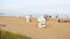 A beach with white wicker chairs and a pier in the background. - Holiday Home in Kappeln (Kappeln)